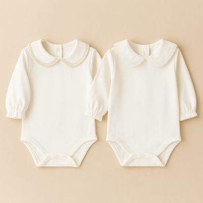 Dois bodies brancos de bebé com mangas compridas e golas de renda, sobre fundo bege.