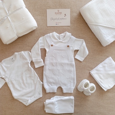 Roupa de bebé branca com cartão de marca DAFRI sobre fundo bege.