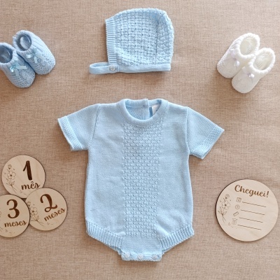 Conjunto de roupa de bebé azul clara com sapatinhos e discos de madeira sobre tecido bege