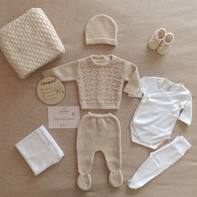 Conjunto de roupa e acessórios de bebê em tons bege e branco sobre superfície bege.