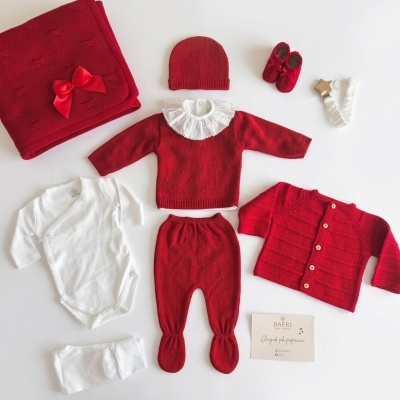 Conjunto de roupa de bebé vermelha e branca com vários artigos dispostos sobre uma superfície branca.