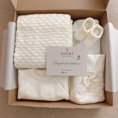 Conjunto de roupa e manta de bebê creme dentro de caixa de papelão com cartão da marca DAFRI