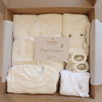 Conjunto de roupa de bebé creme e branco numa caixa com cobertor, casaco, sapatinhos, body e peça de malha