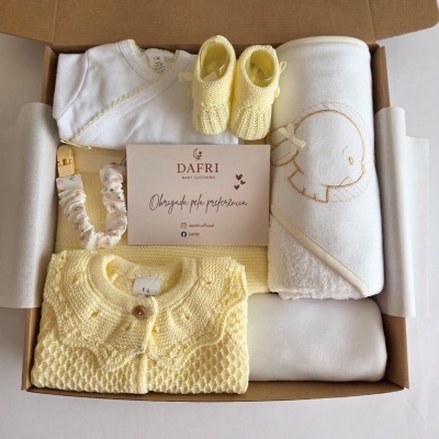 Conjunto de roupa de bebé com casaco amarelo, sapatinhos amarelos, bodie branco, manta branca com bordado de elefante numa caixa de cartão