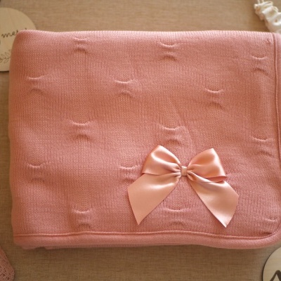 Manta de malha rosa com laço de cetim e acessórios de bebé em fundo bege