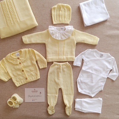 Conjunto de roupa de bebé amarelo e branco sobre superfície bege