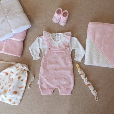 Conjunto bebê rosa e branco com sapatinhos, manta, bolsa e faixa de cabelo sobre tecido bege