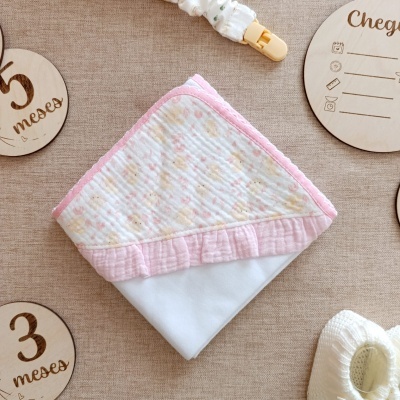 Fralda branca com borda rosa e flores, marcadores de idade para bebés em fundo bege.