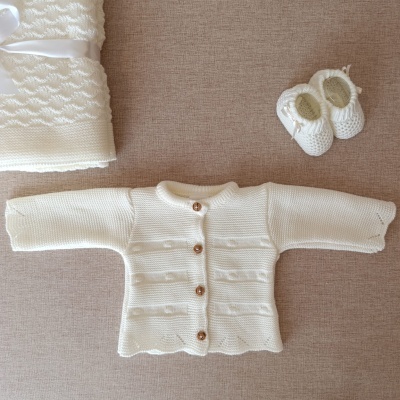 Conjunto de bebé creme com camisola, sapatinhos e manta em malha texturada.
