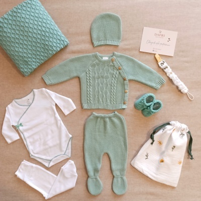 Conjunto de roupa de bebé em tricô e algodão com diversos acessórios e embalagem branca com padrão floral