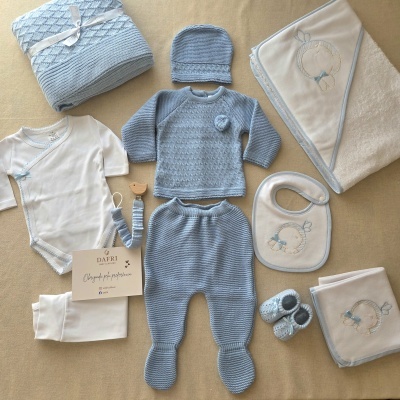 Conjunto de roupa de bebé azul e branco com mantas e babetes bordados, sobre fundo bege.