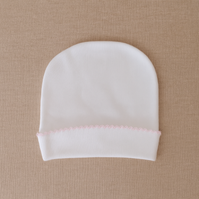 Gorro de bebé branco com bordado rosa sobre fundo bege.