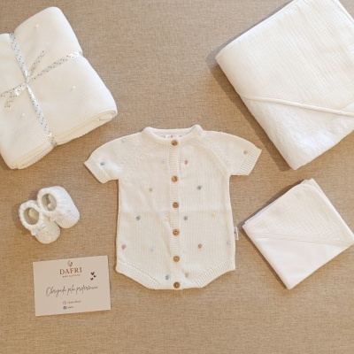 Conjunto de roupa e acessórios para bebé branco com pontos coloridos e botões de madeira sobre superfície castanha