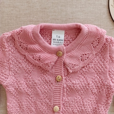 Camisola ou casaquinho de malha rosa com botões de madeira e etiqueta visível.