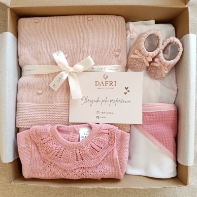 Conjunto de roupa de bebé em caixa de cartão com vários itens em tons de rosa e branco e cartão da marca DAFRI