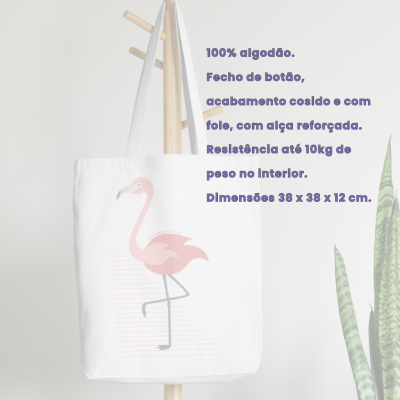 Saco branco de algodão com estampa de flamingo rosa pendurado num cabideiro ao lado de plantas