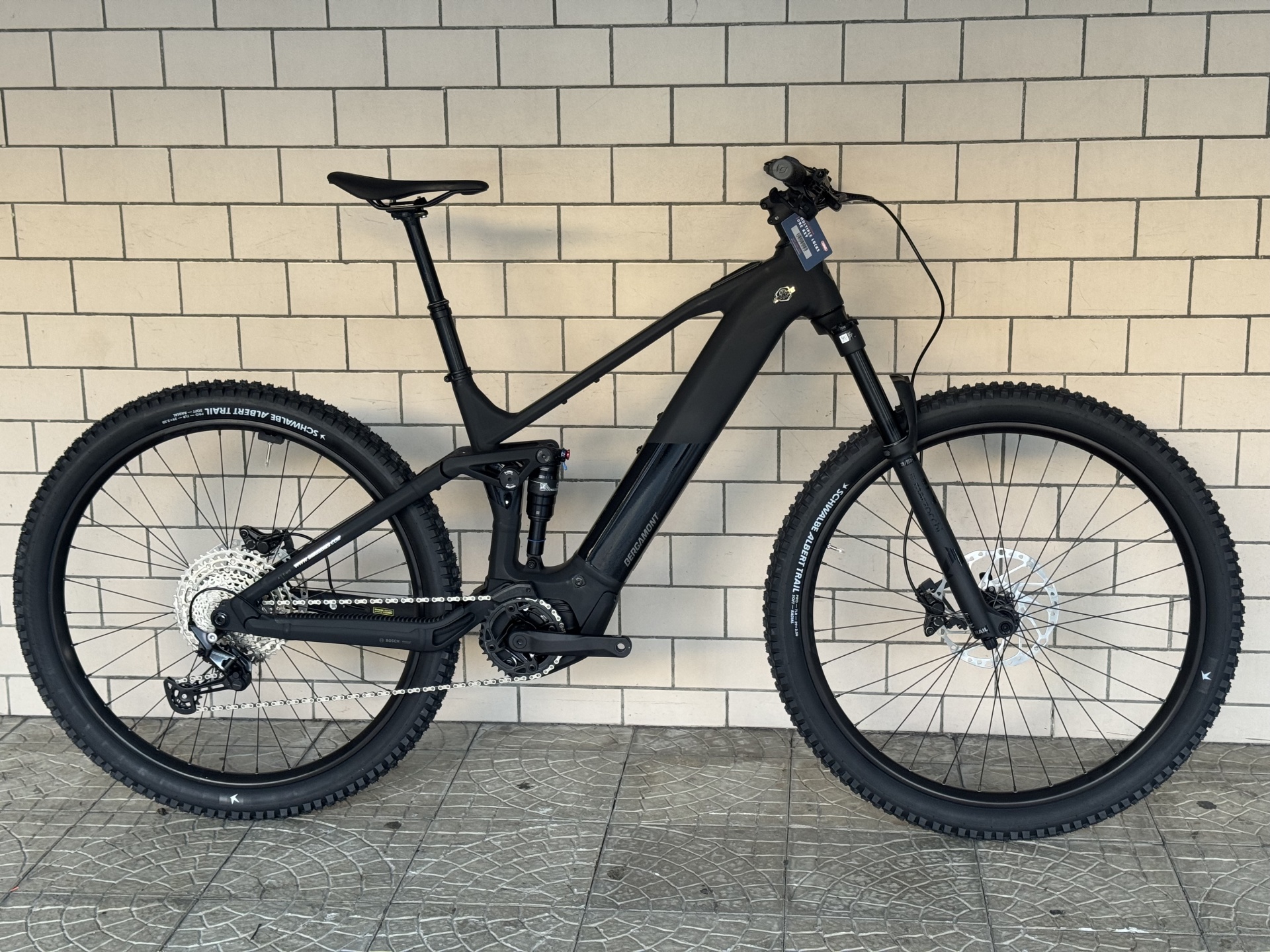 BICICLETA ELÉTRICA BERGAMONT E-REVOX FS 20 Bicicleta elétrica de montanha BERGAMONT preto mate junto a parede de azulejos brancos