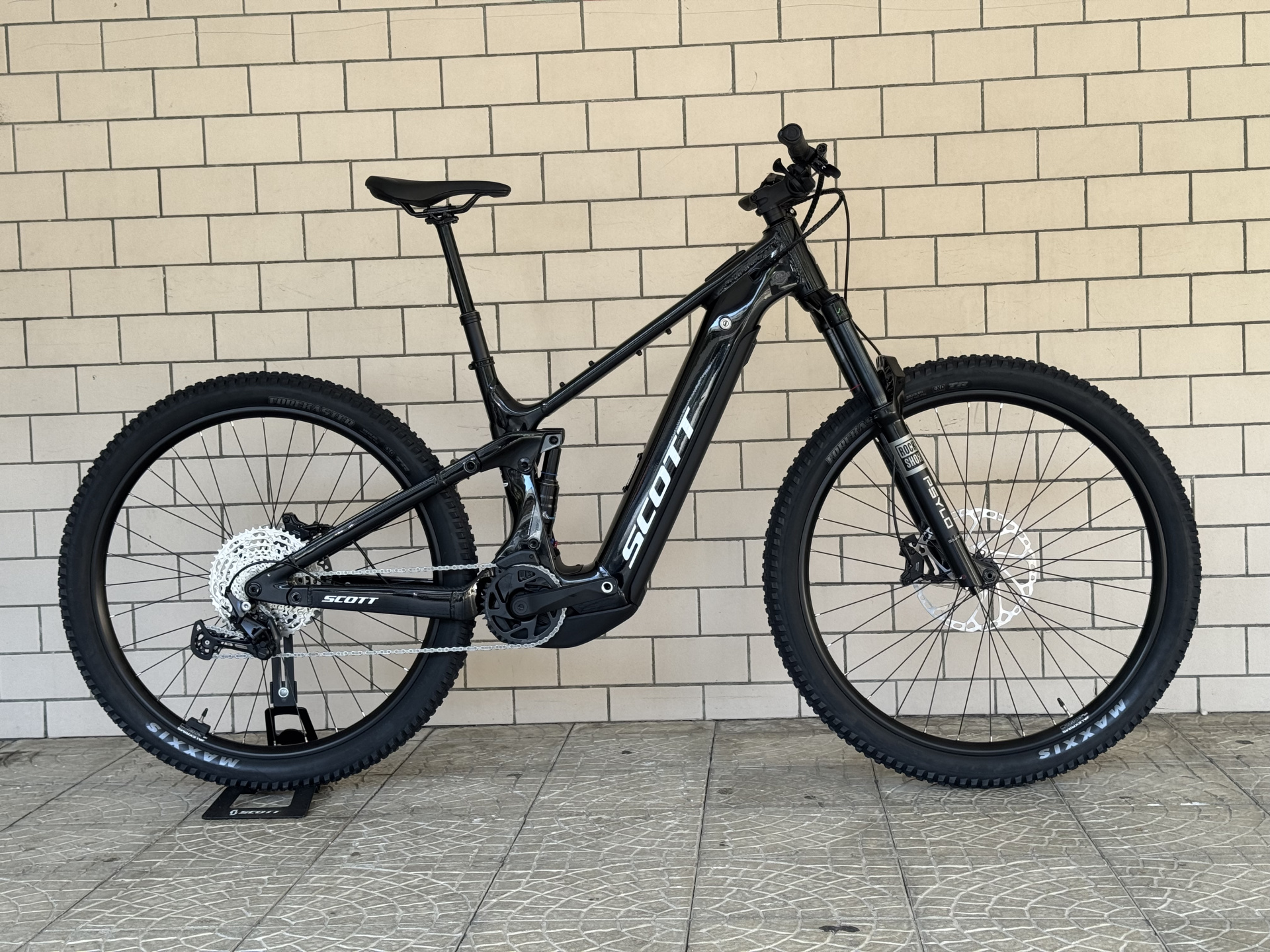 BICICLETA ELÉTRICA SCOTT STRIKE 30 - BLACK Bicicleta de montanha elétrica preta SCOTT contra parede de azulejos
