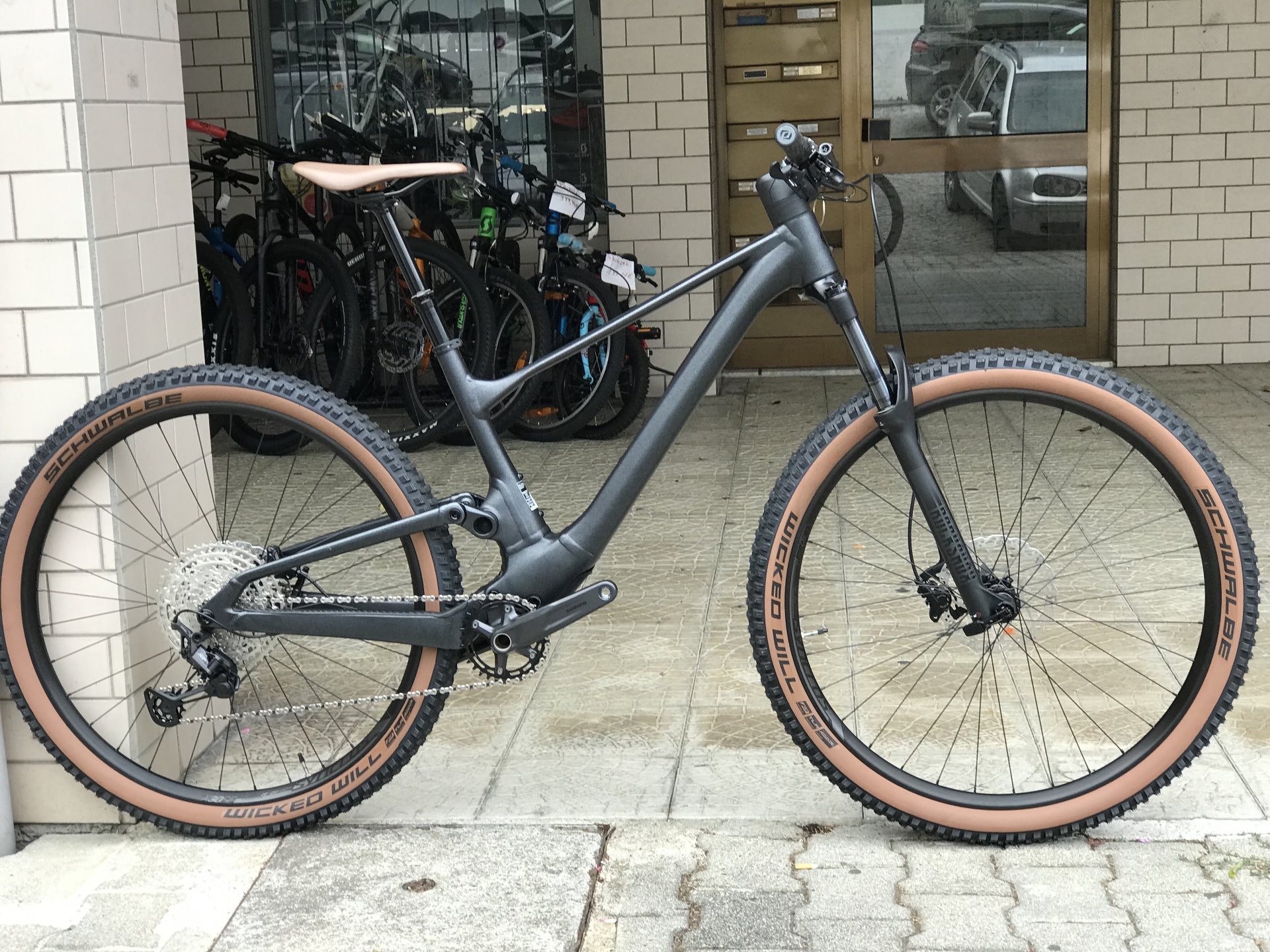 BICICLETA SCOTT SPARK 960 Black - 2024 Bicicleta de montanha elétrica cinza com pneus castanhos no pavimento de pedra em frente a um prédio