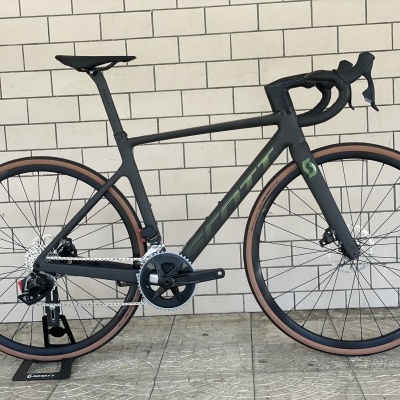 Bicicleta de estrada preta com pneus castanhos claros encostada numa parede de tijolos