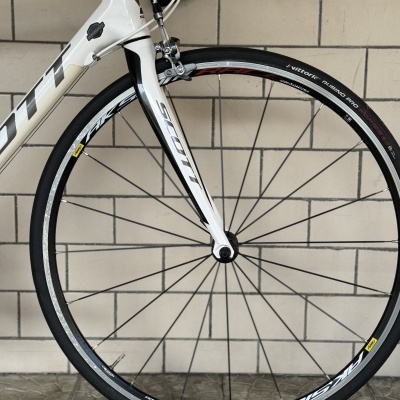 Roda dianteira de bicicleta de estrada branca e preta da marca SCOTT com pneu preto em pavimento