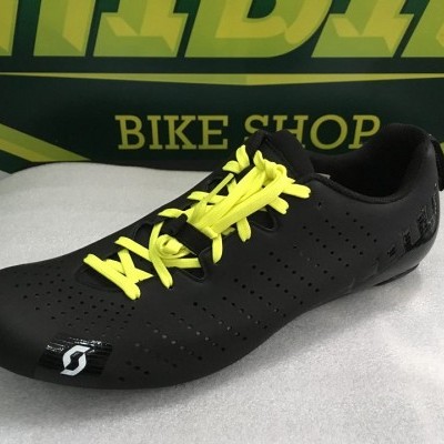 sapato de ciclismo preto com cadarços amarelos em superfície branca