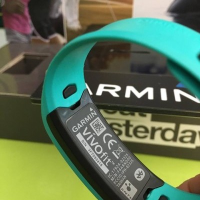 Pulseira desportiva Garmin VivoFit turquesa com etiqueta preta e caixa de fundo.