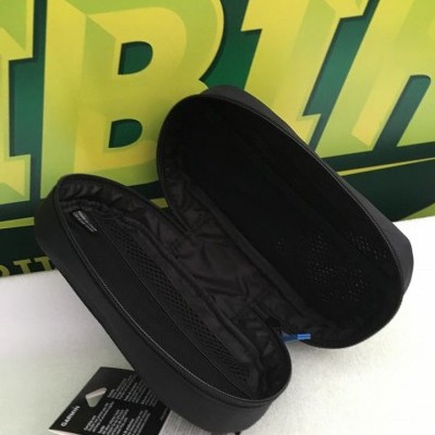 Estojo preto aberto com interior preto e bolsos de rede, etiqueta pendurada e fundo verde com letras amarelas