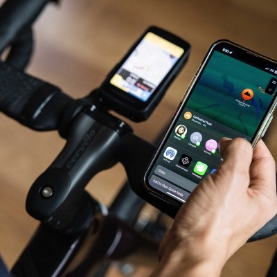 Guiador de bicicleta com ciclocomputador Garmin e mão segurando smartphone com várias aplicações