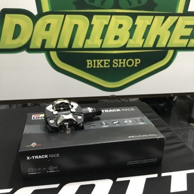 Pedal de bicicleta X-TRACK RACE sobre caixa preta diante de placa DANIBIKES BIKE SHOP