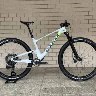 Bicicleta de montanha Scott branca com detalhes verdes e pretos sobre suporte em chão com padrão de ladrilhos