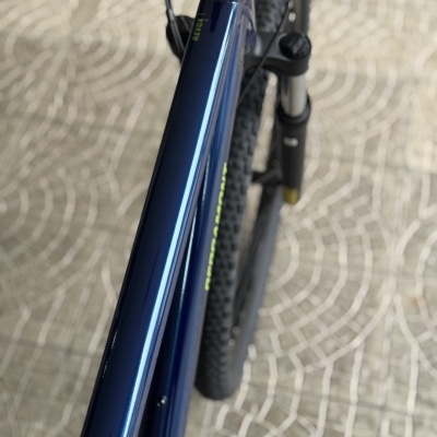 Bicicleta azul metálica com suspensão dianteira, pneus pretos com piso, sobre pavimento de pedras onduladas