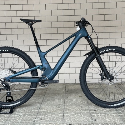 Bicicleta de montanha elétrica azul com pneus Maxxis à frente de parede branca