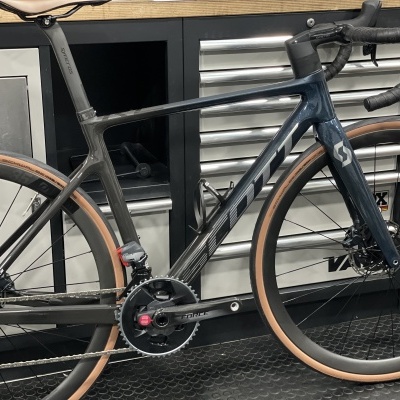 Bicicleta de estrada preta com logótipo SCOTT e pneus castanhos na oficina