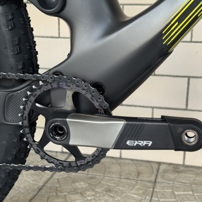Quadro e pedal de bicicleta moderna cinzento e preto com detalhes amarelos junto a uma parede de azulejo bege