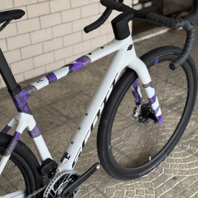 Bicicleta de estrada branca com detalhes roxos apoiada em chão com ladrilhos