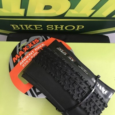 Pneu de bicicleta Maxxis Ardent Race com padrão de piso, em suporte vermelho e preto, sobre superfície amarela