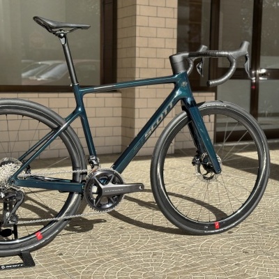 Bicicleta de estrada azul metálico apoiada num terraço com parede de tijolos claros e portas de vidro