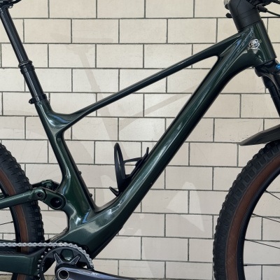 Quadro de bicicleta de montanha verde escura com garfo e selim pretos, pneus castanhos, logótipo DADIBIKES, parede de azulejos brancos