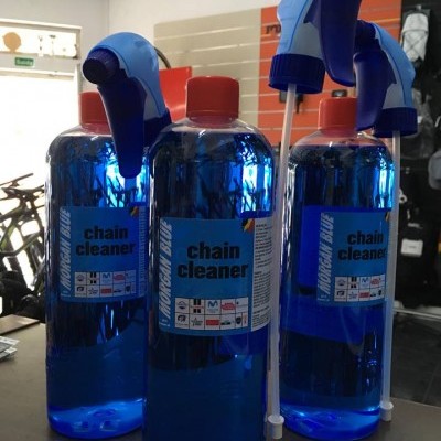 Três frascos de chain cleaner azuis com tampas vermelhas e bicos borrifadores em loja de bicicletas