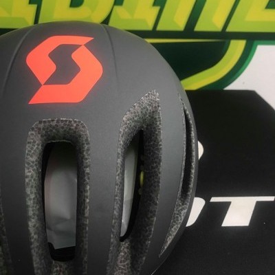 Capacete de ciclismo cinza com logótipo laranja da Scott e entradas de ar