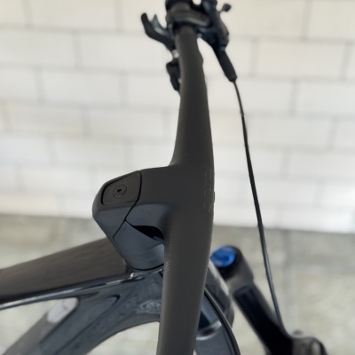 Bicicleta com guiador preto mate e quadro cinza metálico perto de parede branca.