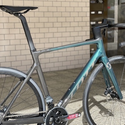 Bicicleta de estrada cinza e azul metálico encostada a parede de tijolos brancos