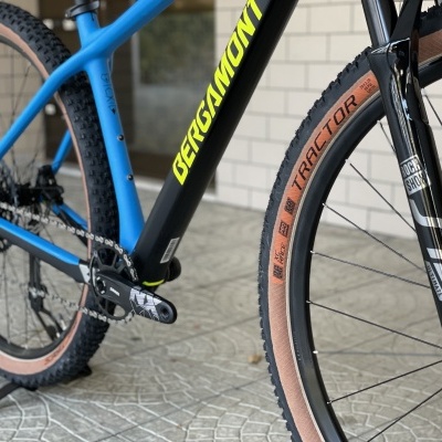 Detalhe de bicicleta de montanha azul e preto com pneus castanhos numa superfície de azulejo cinzento