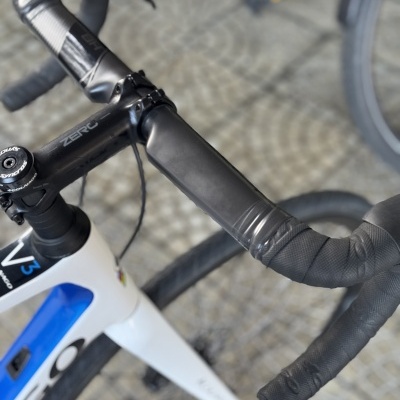 Guidão de bicicleta de estrada preto com fita preta montado numa bicicleta branca e azul