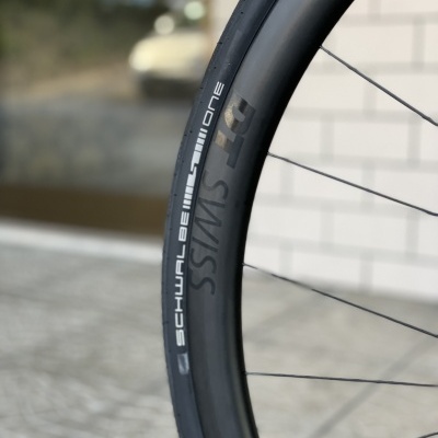 Roda de bicicleta com aro preto DT Swiss e pneu Schwalbe One em ambiente urbano