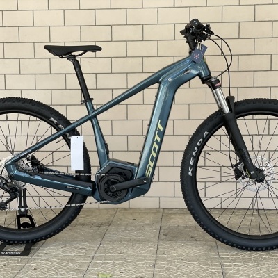 Bicicleta elétrica azul com motor central e pneus pretos Kenda contra parede de blocos de cimento