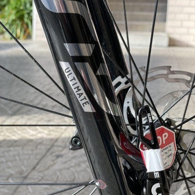 Garfo de bicicleta preto com texto ULTIMATE e selo STOP próximo à roda dianteira