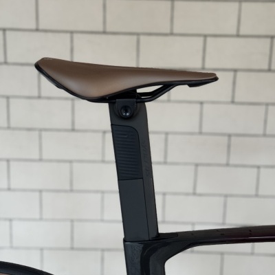 Selim castanho de bicicleta e estrutura preta com parede de azulejos cinzentos ao fundo