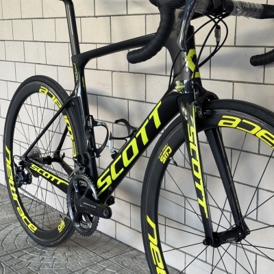 Bicicleta de estrada Scott preta e amarela contra parede de azulejos brancos